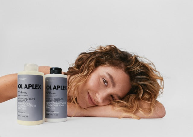 A woman with wavy hair in front of No.4CURL Bond Shaper™ Hydrating Curl Shampoo and No.5CURL Hydrating Curl Conditioner