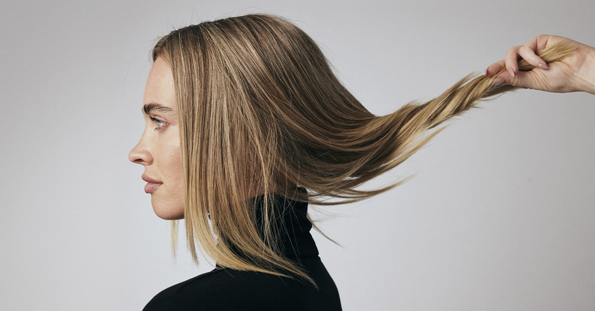 Woman with blonde, straight hair being gently twisted by a hand 