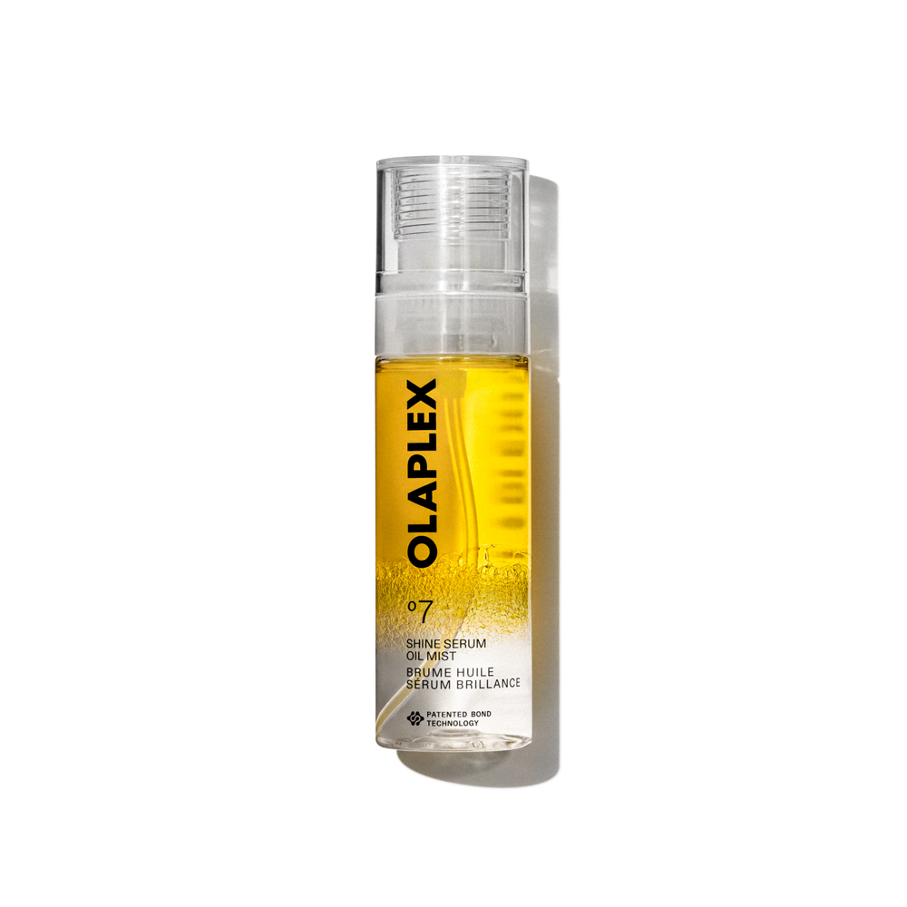 Imagen de producto del Olaplex No. 7 Shine Serum Oil Mist en un pulverizador transparente de 80 ml. La botella contiene un líquido amarillo brillante visible en su interior, una tapa transparente y una etiqueta blanca limpia en la parte inferior con texto negro que muestra el nombre del producto, los detalles y la firma “No.” Logotipo de 7". La botella aparece aislada sobre un fondo de cuadrícula transparente. - main view