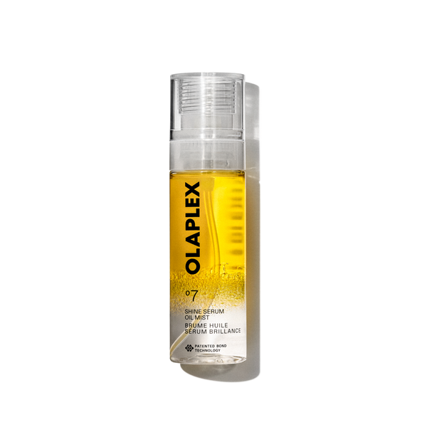 A product packshot of Olaplex No. 7 Shine Serum Oil Mist in an 80ml clear spray bottle. The bottle features a bright yellow liquid visible inside, a transparent cap, and a clean white label at the bottom with black text displaying the product name, details, and the signature "No. 7" logo. The bottle is isolated against a transparent grid background. - main view